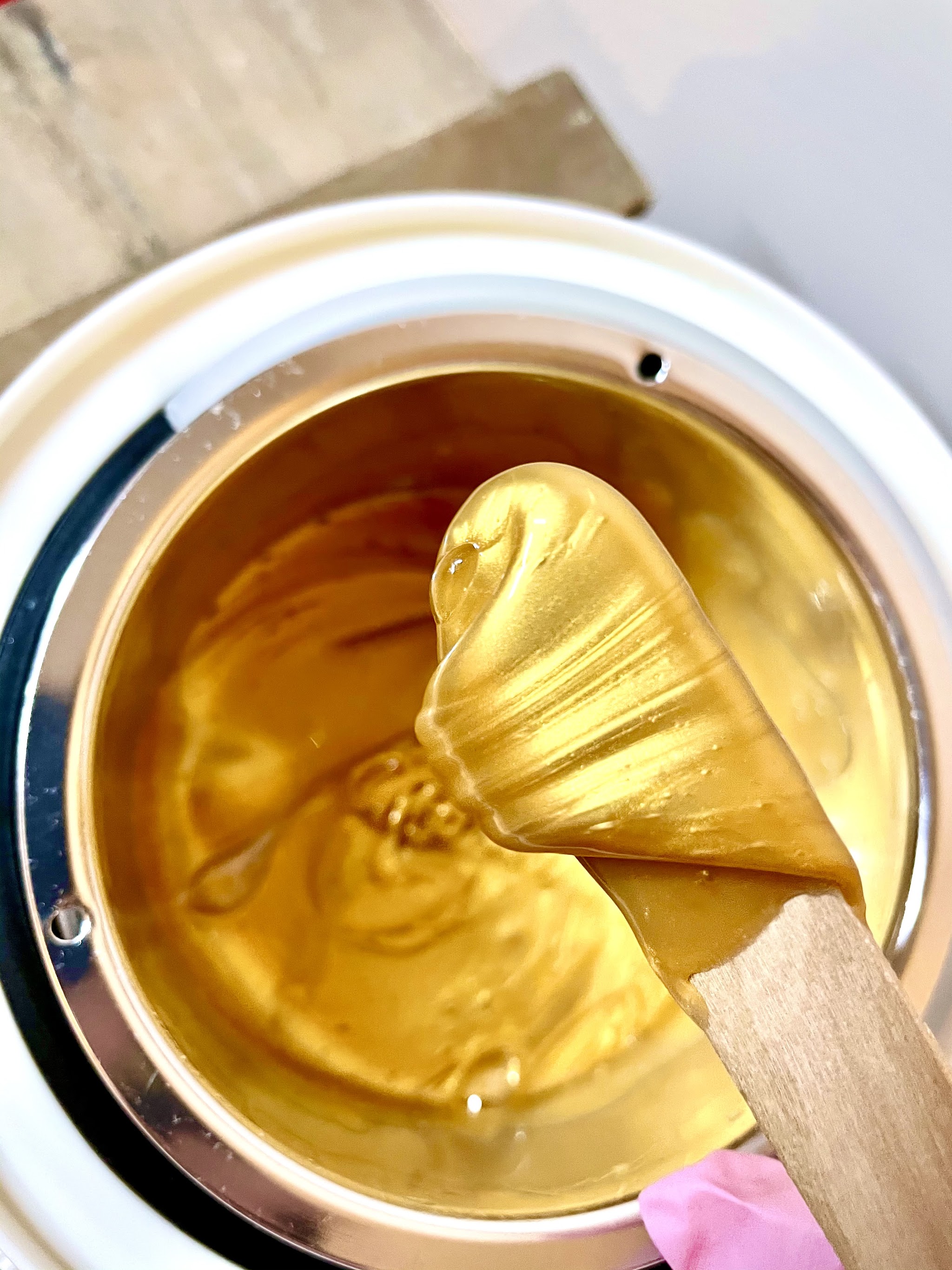 Goudkleurige wax in de waxpot, opgeschept met een houten spatel